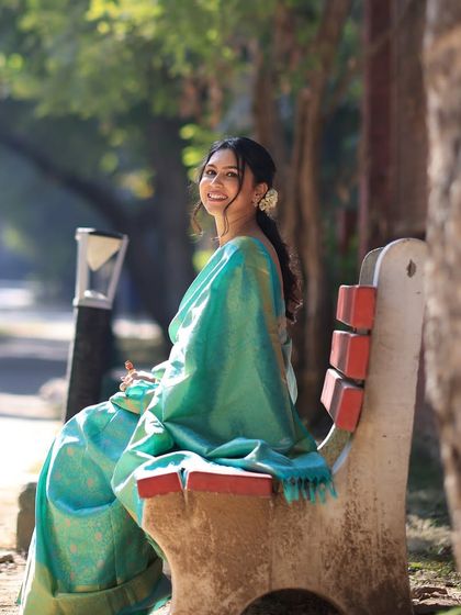 A serene moment captured on a park bench. The bride's natural makeup and the beautiful drape of her saree create a picture of timeless elegance.