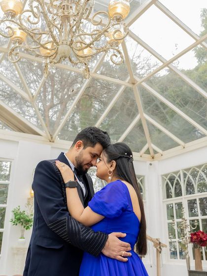 A romantic pre-wedding shot in a beautiful glasshouse setting. The makeup is fresh and radiant, complementing her vibrant blue dress.