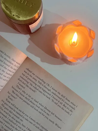 Cozy vibes always. Our orange Daisy Jar candle lit next to an open book, perfect for a relaxing night in.