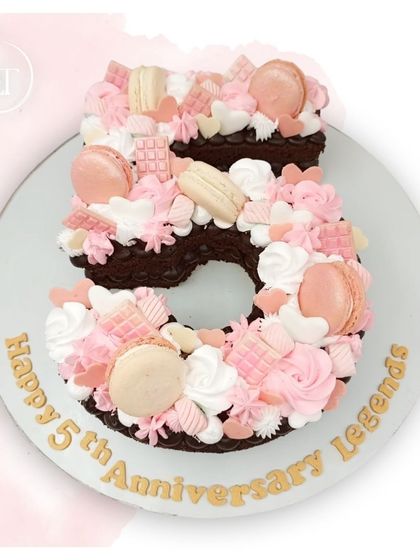 A beautiful number "5" cake for a 5th anniversary, decorated with pink and white macarons, chocolates, and frosting.