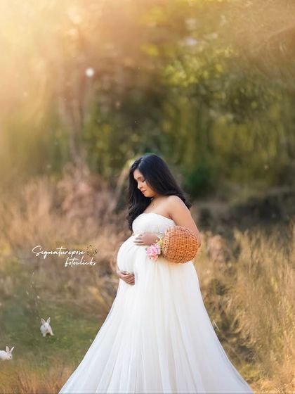 A whimsical and sweet outdoor scene, with the mother-to-be in a white gown surrounded by bunnies and golden light.