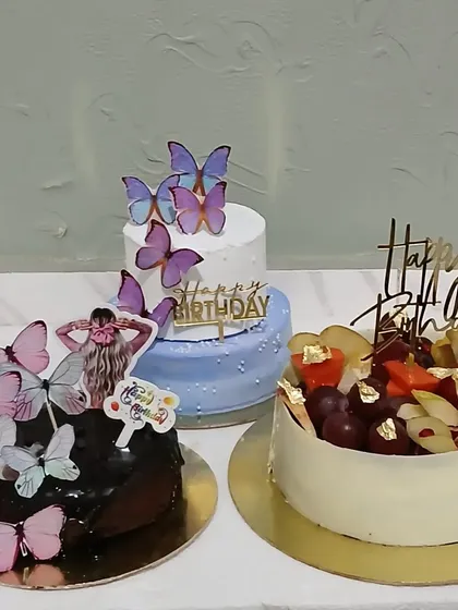 A display of three different birthday cakes: two with butterflies and one with fresh fruit.