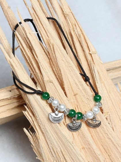 Our "Nazar Ka Dhaga" black thread anklet with green and pearl beads and silver charms. It is adjustable and perfect for daily wear.