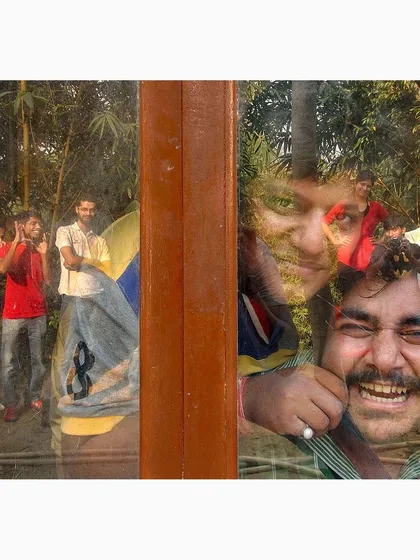 This photograph captures a moment of celebration and friendship, layered through a window reflection. It combines a candid group scene with the intimate, joyful expression of an individual.