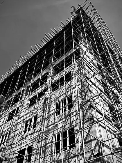 Sleek lines, timeless design. A dramatic black and white shot of a commercial building under construction, its skeleton wrapped in scaffolding.