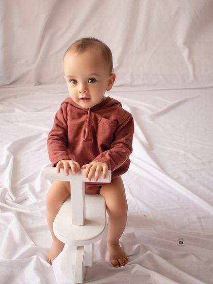 A simple, clean shot of a baby on a wooden tricycle against a white backdrop, highlighting his sweet expression.