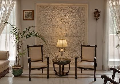 This seating nook in the Kaira residence is a study in texture and light. A large, textured art piece serves as a focal point, flanked by classic chairs and bathed in soft, natural light from sheer curtains, creating a perfect corner for quiet reflection.