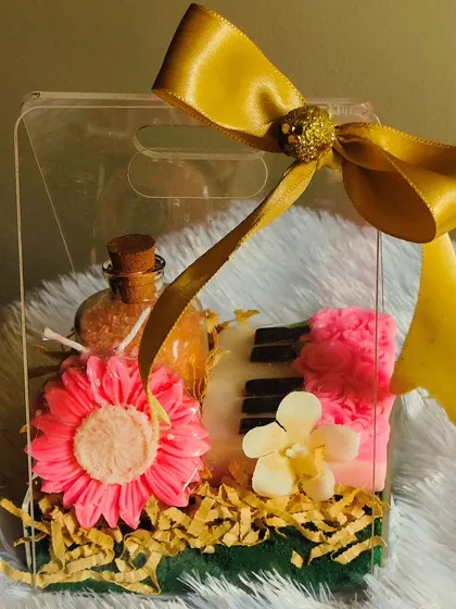 A vibrant gift bag containing a piano soap, flower candles, and muscle-relaxing bath salts, all in a trendy acrylic bag.