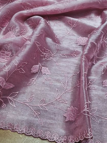 This mauve-pink crush tissue saree drapes beautifully, showcasing the delicate floral embroidery that runs across the fabric. It's a perfect blend of traditional craft and modern sensibility.