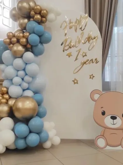 A sweet and simple teddy bear theme for a first birthday, with a blue, white, and gold balloon garland against a clean white backdrop.