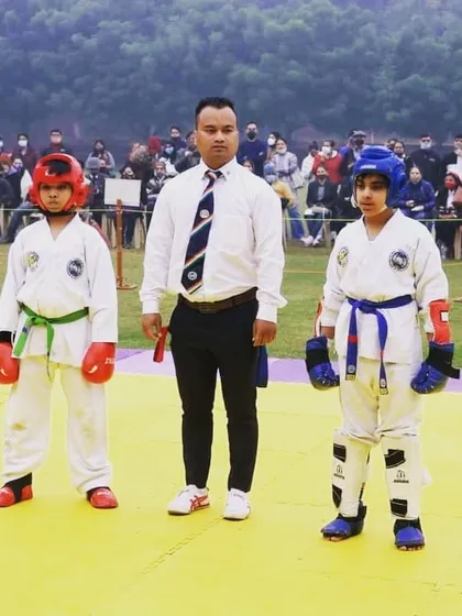Two young competitors facing off before their sparring match begins, with the referee ready. This moment of focus and respect is a core tenet of Taekwondo.