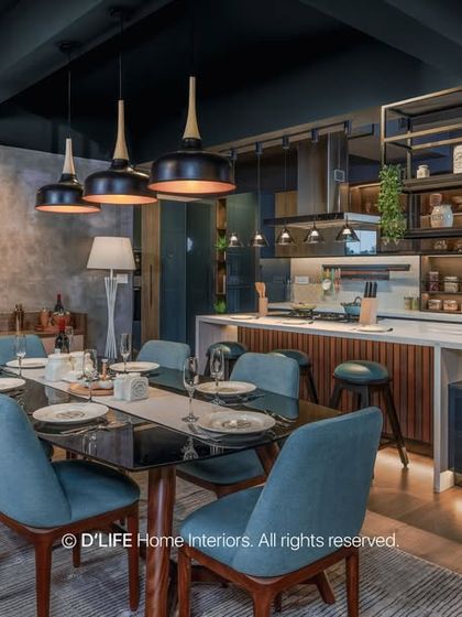 An open-plan dining and kitchen area with a dark, moody aesthetic. The blue dining chairs provide a pop of color, while the industrial lighting adds character.