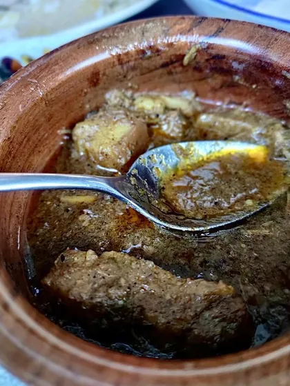 A spoonful of our rich and peppery Pandi Curry. This shot captures the texture of the slow-cooked pork and the dark, luscious gravy, a result of our traditional cooking process and authentic ingredients.