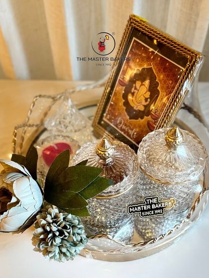 Add a spiritual and personal touch to your gift. This arrangement includes premium dry fruits in crystal jars, a scented candle, and an elegant Ganesha frame, all set on a beautiful silver tray.