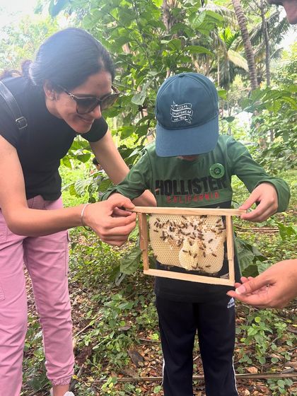 A parent helps her child hold a frame from a beehive, a shared experience of wonder and learning.