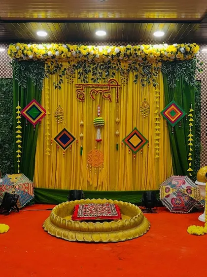 A complete view of a haldi stage setup in a banquet hall. The decor features a green and yellow theme with traditional hangings and a lotus seating area.