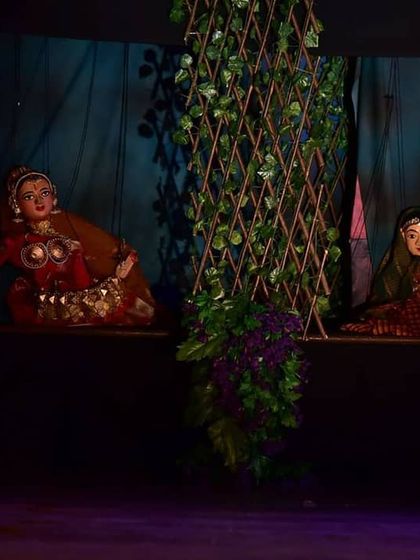 A similar view of the two puppets, emphasizing the intricate stage design with the lattice and foliage.