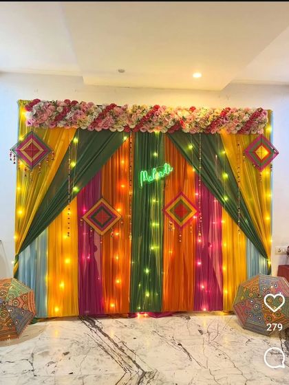 A multi-colored backdrop for a Mehandi night with a neon sign. The setup includes Rajasthani umbrellas and is lit with fairy lights to create a festive and vibrant ambiance.