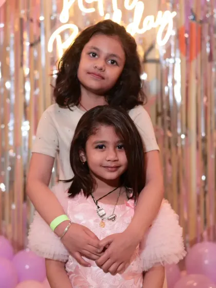 Two sisters posing in front of the birthday backdrop, a beautiful memory of the special day.