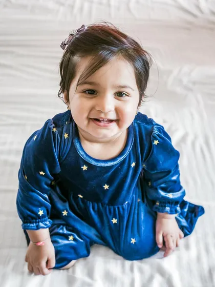 An adorable portrait of a one-year-old girl in a blue velvet dress, looking up with a sweet smile. This shot captures the innocence and charm of early childhood.