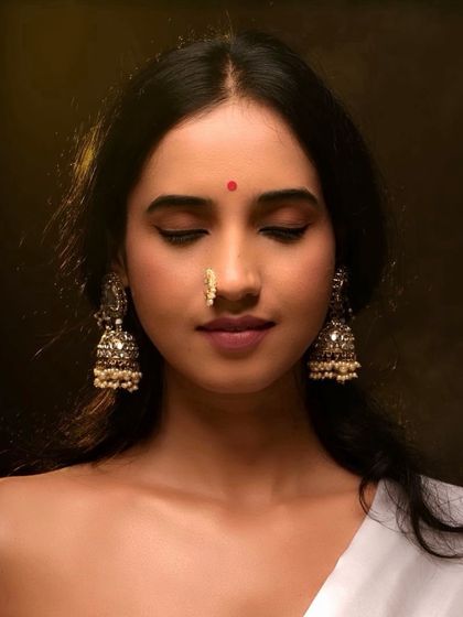A close-up with eyes closed, focusing on the peaceful expression and the exquisite details of the earrings and nose ring.