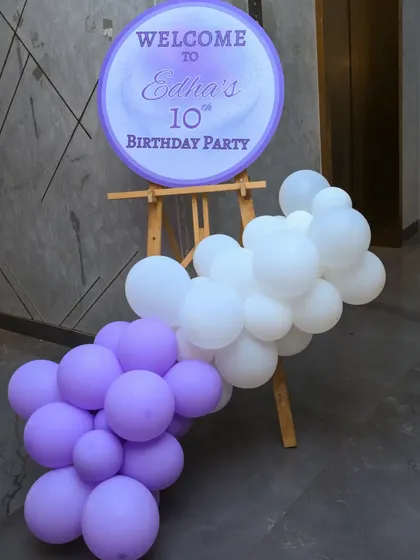 A circular welcome sign on an easel, decorated with a cascade of purple and white balloons, greeted guests at the 10th birthday party.