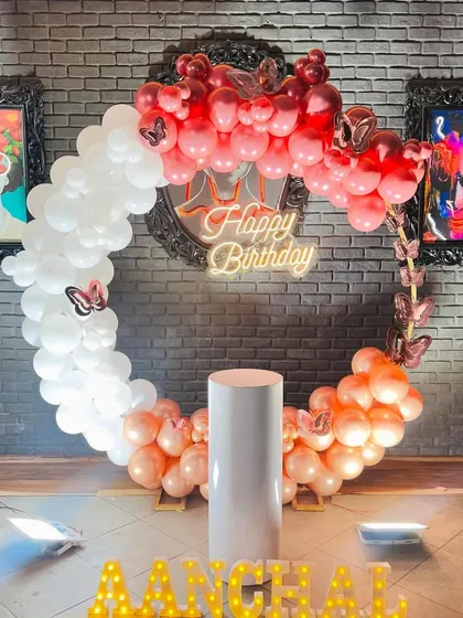 A birthday balloon ring in red, pink, and white set against an industrial-style brick wall, personalized with light-up marquee letters.