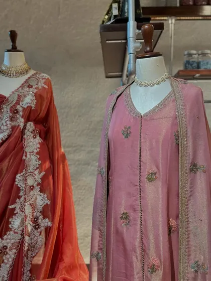 A closer look at the pink suit and the red saree, highlighting the contrast between the detailed figural embroidery and the delicate white lacework.