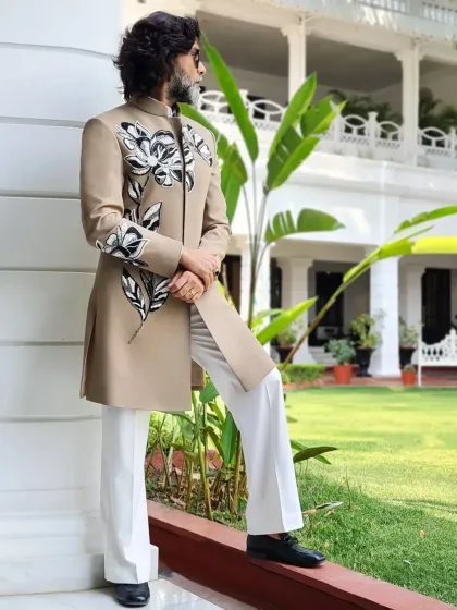 A beige indowestern jacket with bold, black and white hand-painted floral designs, paired with flared white trousers for a retro-inspired, stylish look.