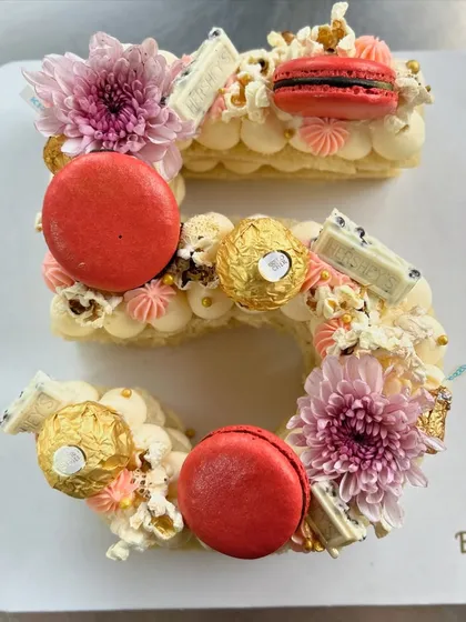 A close-up of the number '5' monogram cake, showing the beautiful arrangement of macarons, chocolates, and fresh flowers.