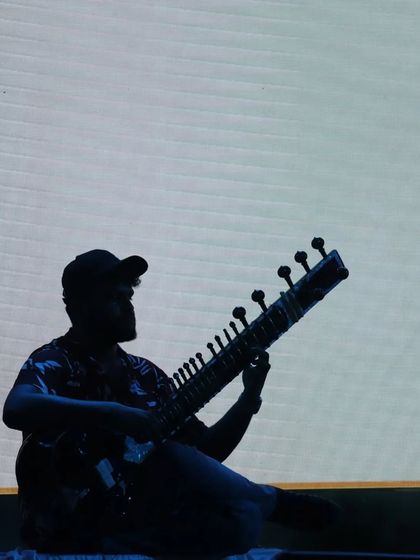 A striking silhouette against a simple white background. This artistic shot highlights the iconic shape of the sitar and the player.