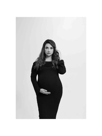 A striking black and white portrait against a clean white background. The simplicity of the shot puts all the focus on the mother-to-be's confident pose and her connection with her baby.