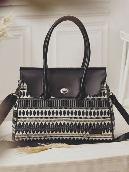 A beautifully styled shot of a patterned handbag in a lifestyle setting, using props like dried grass to create an earthy, elegant mood.