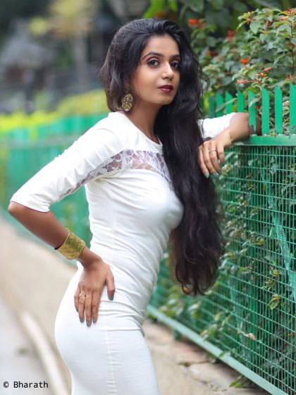 A confident pose against an urban fence. The combination of the white dress and green background creates a fresh, clean look.