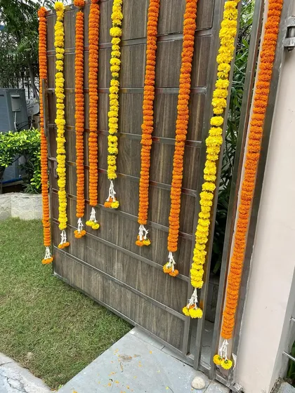 This is a closer view of a main gate decorated with alternating lines of orange and yellow marigold garlands. This dense floral arrangement is perfect for making a statement during important festivals or company celebrations.