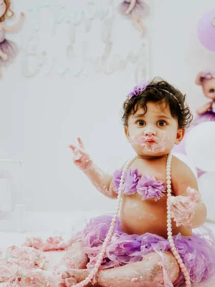 Holding up two messy fingers, maybe signaling she's ready for round two. The pearl necklace adds a fun, dress-up element to the shoot.