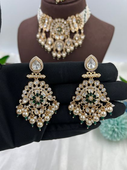 The Ziva Premium Moissanite Kundan Necklace. This choker set is defined by its floral-inspired motifs, pearl droppings, and a matching maang tikka, available in both red and green stone options.