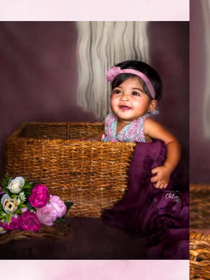 This little girl peeks out of a wicker basket with a sweet smile. The rich, warm tones of the backdrop and props give this studio portrait a cozy and timeless feel.