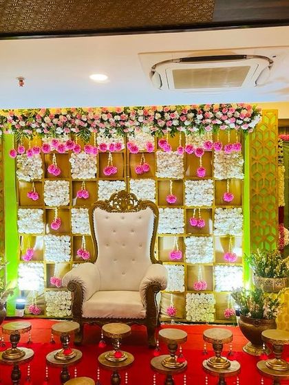 A beautiful pink and white themed backdrop for a baby shower. The checkerboard design is made with panels of white flowers, accented by hanging pink floral tassels for a delicate and feminine touch.