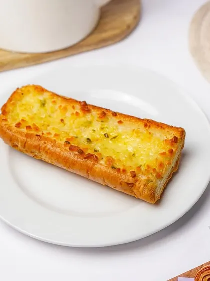A single piece of cheesy garlic bread on a white plate, with a golden fork nearby. The simple, clean presentation makes this popular appetizer look delicious and ready to eat.