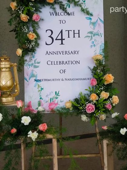 A personalized welcome sign for a 34th-anniversary celebration, beautifully framed with fresh flowers and a vintage-style lantern.