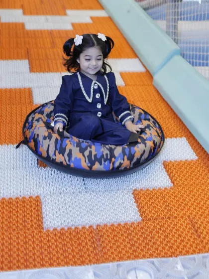 A stylishly dressed child enjoys a gentle ride down the Donut Slide.