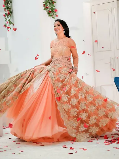 A happy client twirls in a flowing peach gown by Shantanu & Nikhil, perfect for a pre-wedding shoot or reception party. This designer rental gown features delicate lacework over a lightweight tulle skirt.