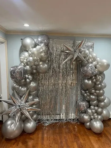 A disco-themed silver tinsel backdrop framed with a silver balloon arch and star-shaped balloons, perfect for a sangeet or New Year's party.