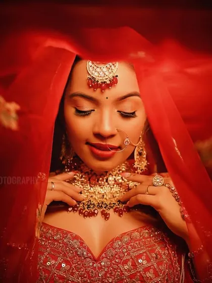 A classic bridal portrait with the bride looking down, framed by her red veil. The lighting creates a timeless and elegant mood.