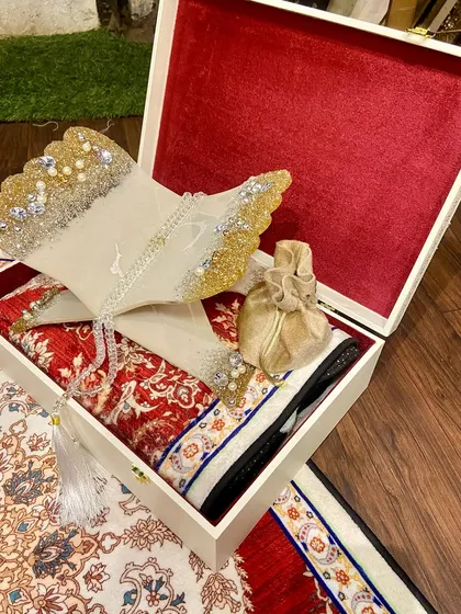 A complete Ramadan gift box, ready to be presented. This set includes a dome-shaped prayer mat with a traditional red and white pattern, a resin Quran holder, a crystal tasbeeh, and a decorative gift box.