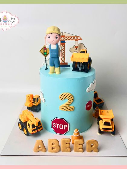 Caution: cuteness under construction! This single-tier construction cake for a 2nd birthday is surrounded by toy trucks and features a friendly fondant construction worker on top.