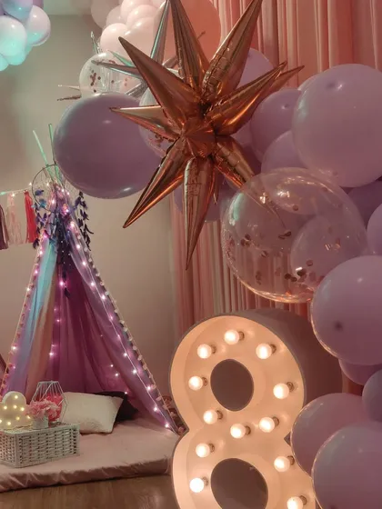 Creating a magical atmosphere is key for a slumber party. A large light-up number '8' and a metallic starburst balloon add a touch of sparkle and fun to the teepee and balloon arrangement.