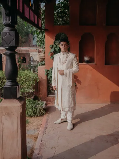 A handsome portrait of the groom at Neemrana Fort, his off-white sherwani standing out against the warm, rustic tones of the palace walls.