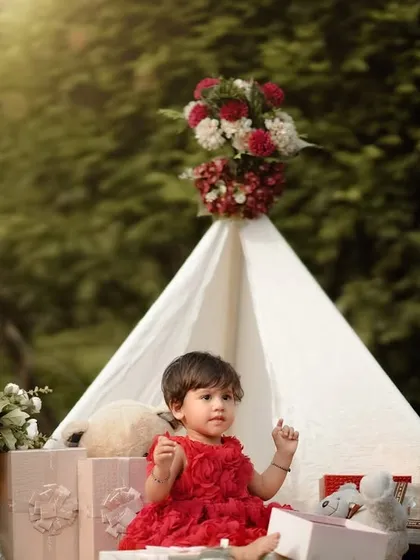 A little princess in her garden castle. This beautiful teepee setup, adorned with flowers and surrounded by presents, is perfect for a first birthday celebration.